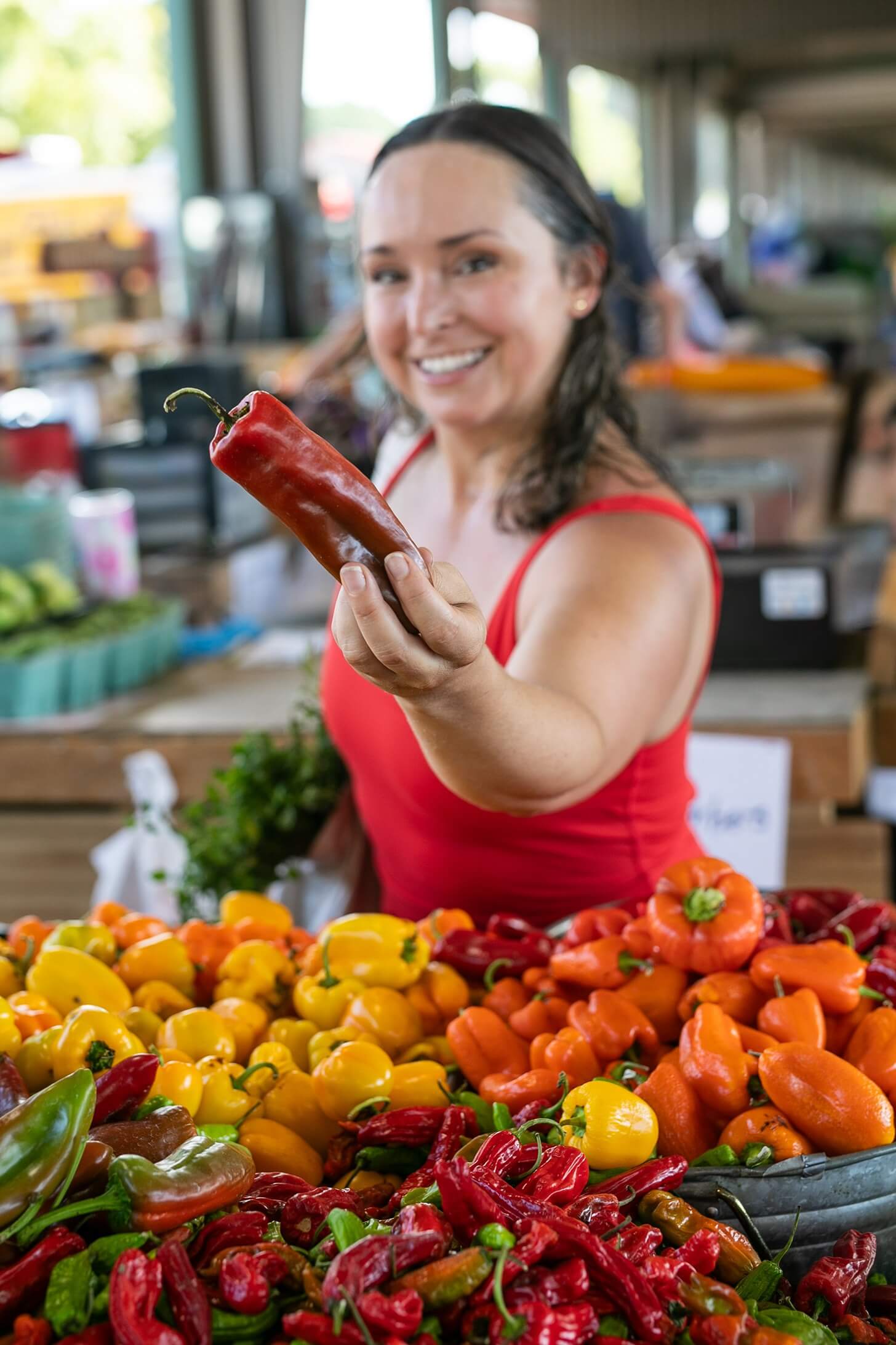 Fitness coach, Coach Lil at Raleigh's Farmers market holding up a red pepper.